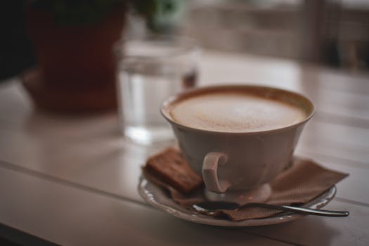 A close-up shot of a cappuccino with a biscuit on a napkin indoors, creating a warm ambiance.