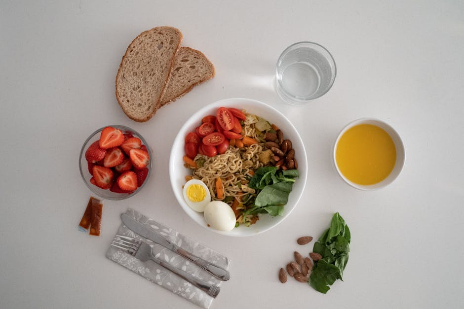 A balanced meal featuring a variety of healthy ingredients including noodles, eggs, almonds, strawberries, and fresh vegetables.
